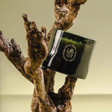 Black candle with a logo on a wooden branch against a beige background