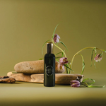 Black bottle with gold cap on a green background with stones and flowers