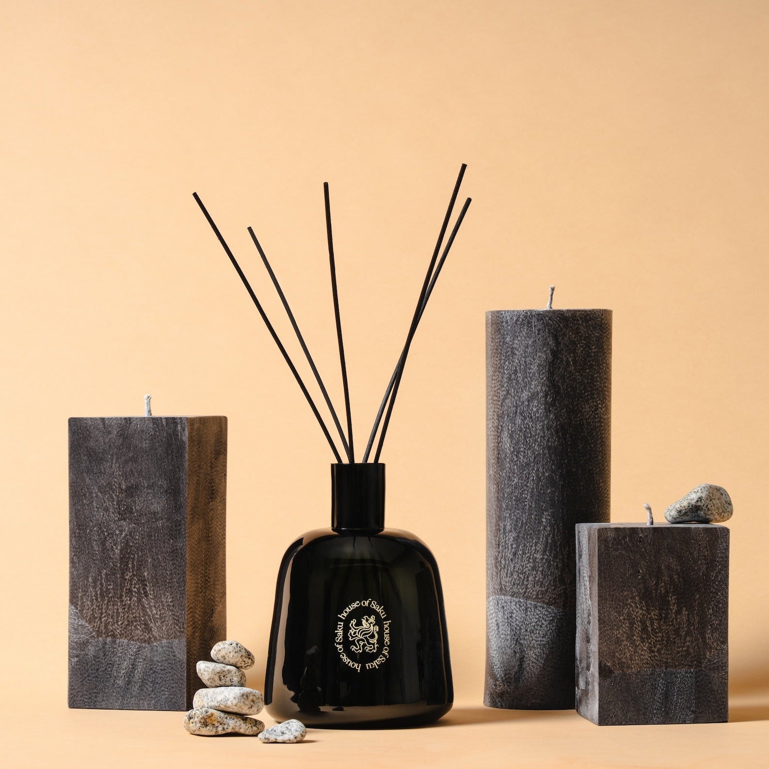 Black diffuser bottle with sticks, candles, and stones on a beige background