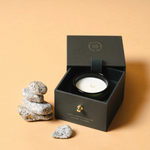 Candle in a black box with decorative stones on a beige background